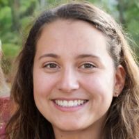 Smiling young woman with long brown hair in an outdoor close-up portrait against a leafy green background